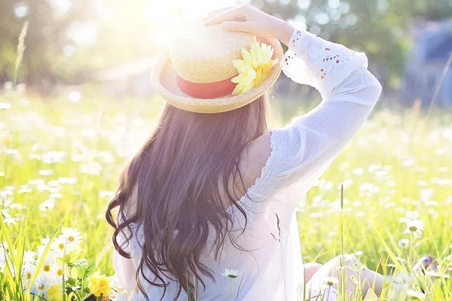 Woman in a field of flowers wearing a straw hat with a red ribbon and a flower celebrating the Spring Equinox