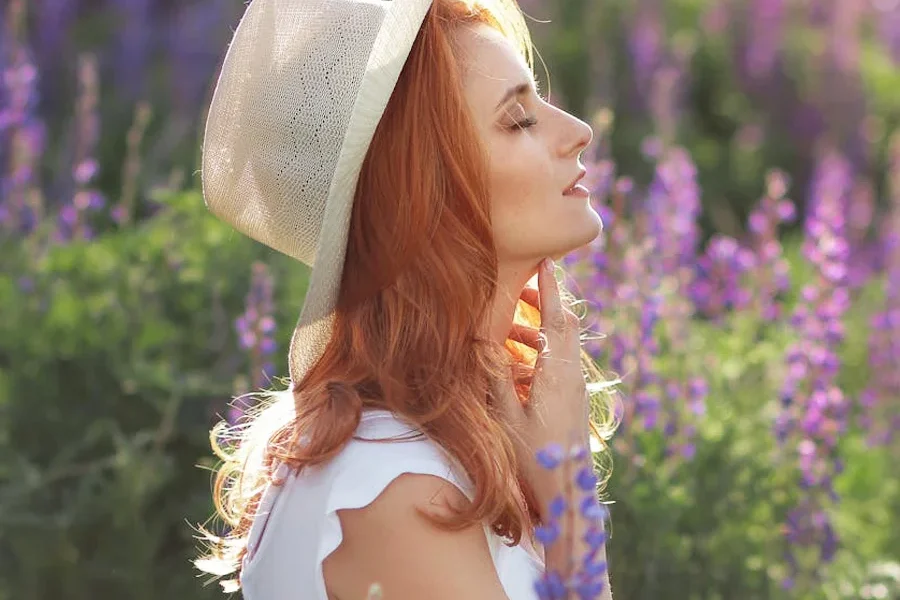Woman with red hair wearing a white hat doing er gardening in a field of purple flowers