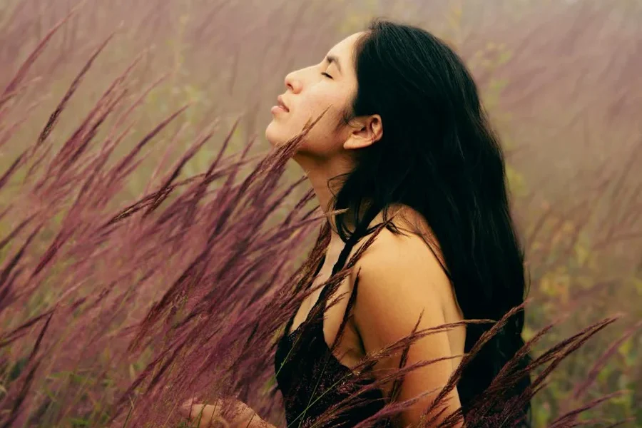 Young woman standing in a meadow with her face turned to the sky and eyes closed